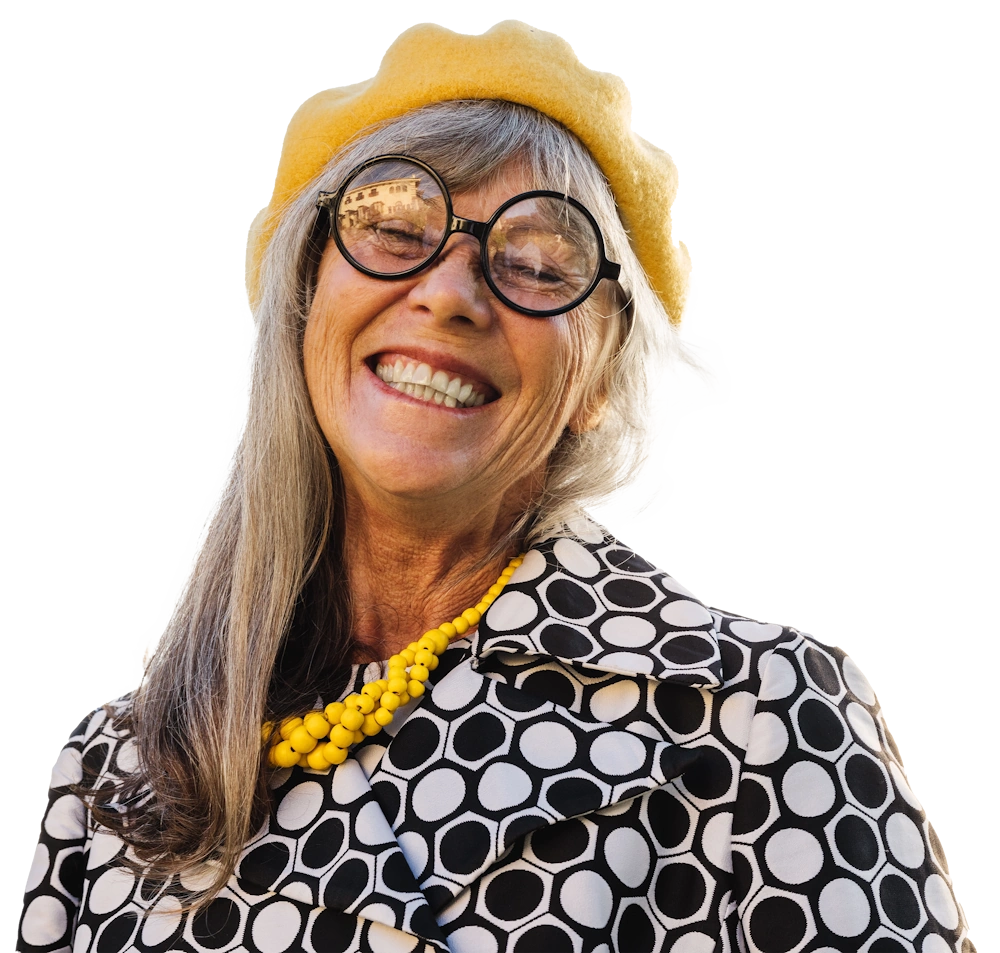 Woman with grey hair, glasses, and a yellow beret smiling 